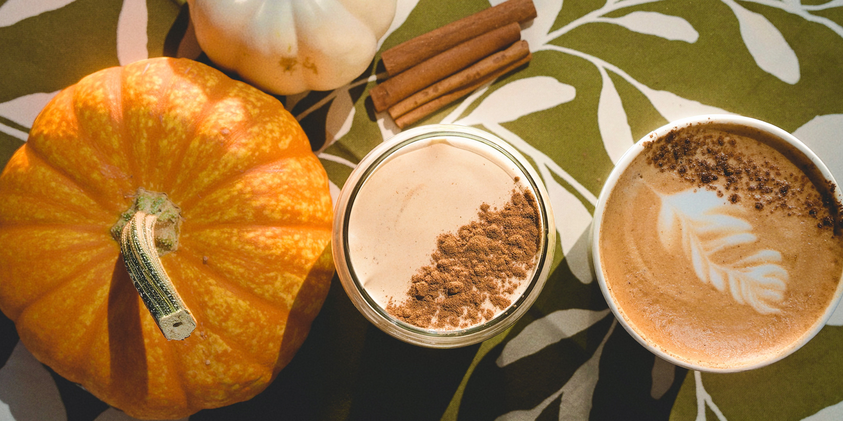 Pumpkin patch lattes dusted with cinnamon beside a pumpkin and cinnamon sticks